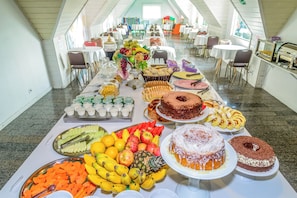 A buffet table with various fruits, pastries, and cakes in a spacious room with tables and chairs. - Pousada Parque das Flores (Campos do Jordão)