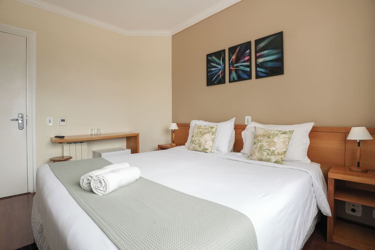 Habitación de hotel con una cama bien hecha, una mesita de noche con lámpara y una obra de arte en la pared.