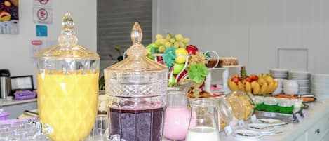 Montaje de buffet con diversas opciones de comida y bebida, incluyendo una exhibición de frutas y dispensadores de líquidos.