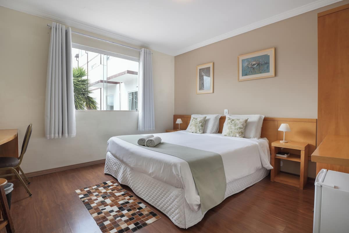 Habitación de hotel con una cama grande, un escritorio, una silla, una mesita de noche y una ventana con cortinas.