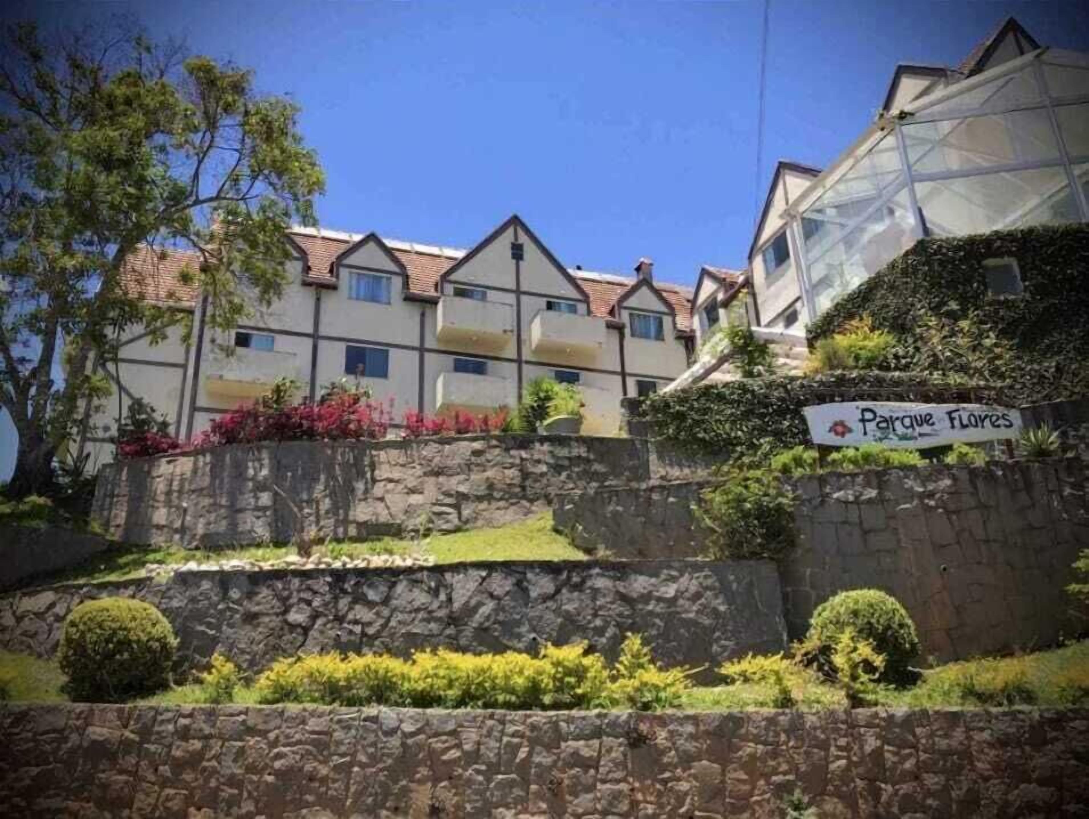 A row of residential buildings with a stone wall and a sign that reads "Parque Flores".