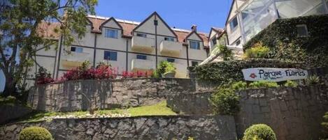 A row of residential buildings with a stone wall and a sign that reads "Parque Flores".