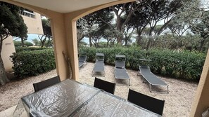 An outdoor patio with a covered table and chairs, surrounded by greenery and trees.