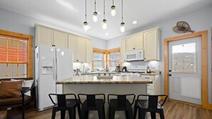 A modern kitchen with a central island, bar stools, and a dining area with a brown sofa. - 3BR 2.5BA Mnt Views! Hot Tub/Pool Table! 2mins to downtown! (Gatlinburg)