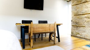A room with a wooden table and chairs, a flat-screen TV mounted on the wall, and a stone wall. - Stunning spacious apt in culross (culross, fife)