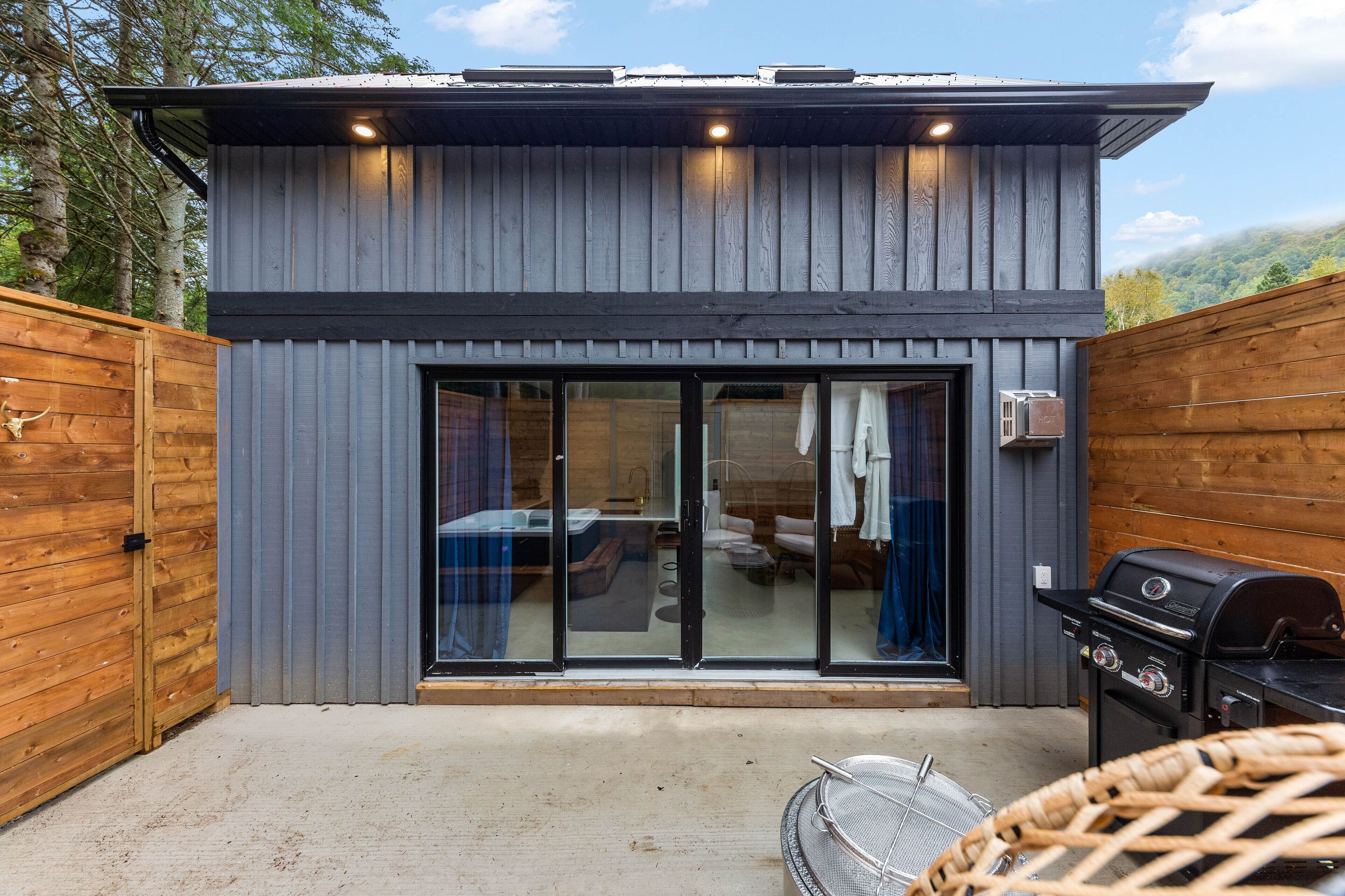 A modern building with a large sliding glass door, a barbecue grill, and a wicker chair.
