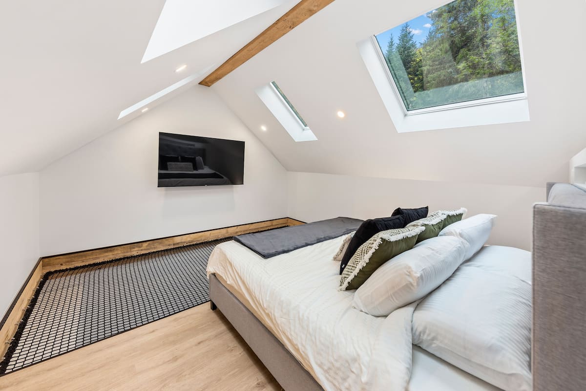 Une chambre de style loft moderne, avec un plafond en pente, un puits de lumière et un téléviseur intégré.