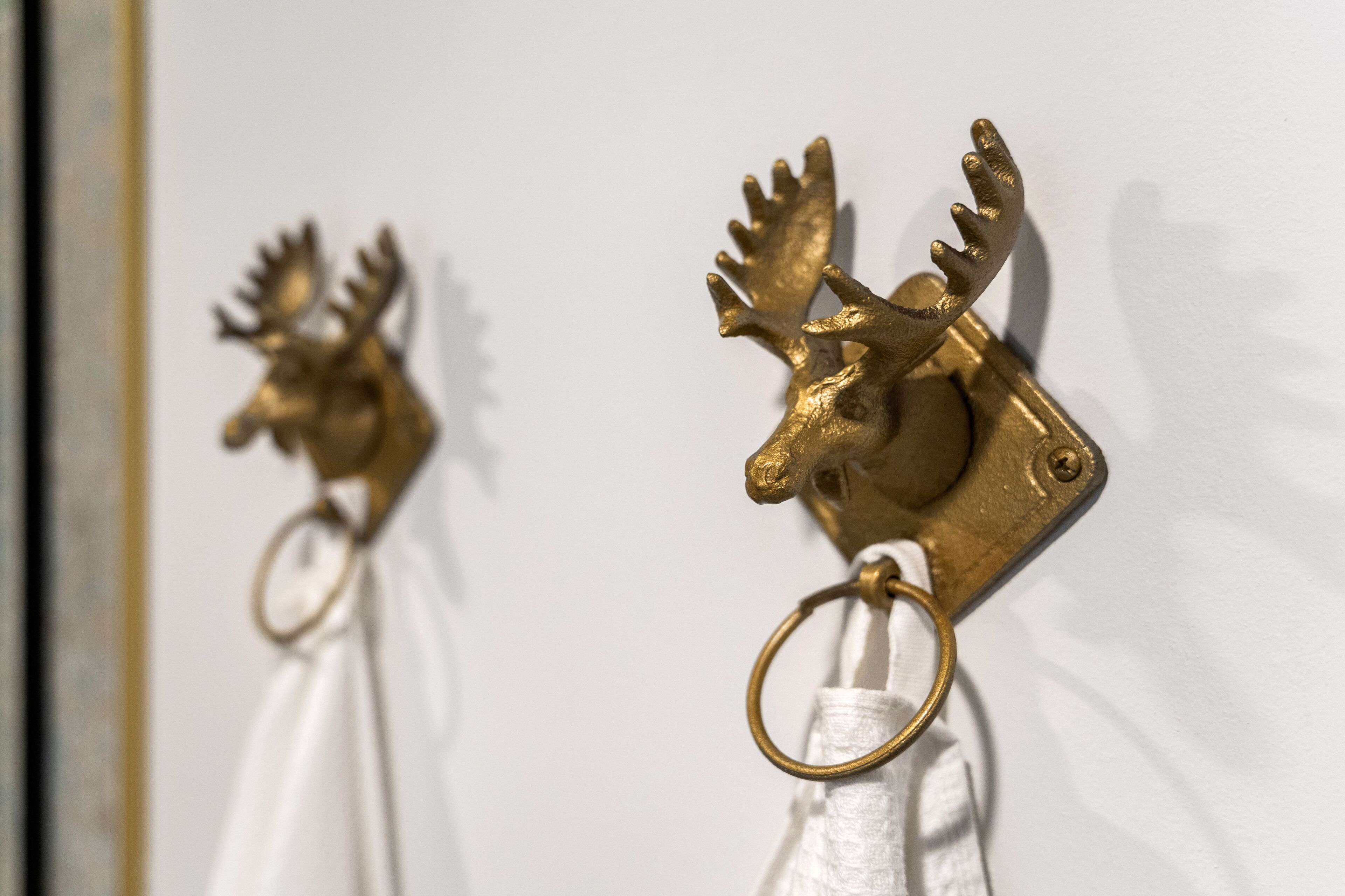 A close-up of a brass moose head mounted on a wall, attached to a white towel ring.