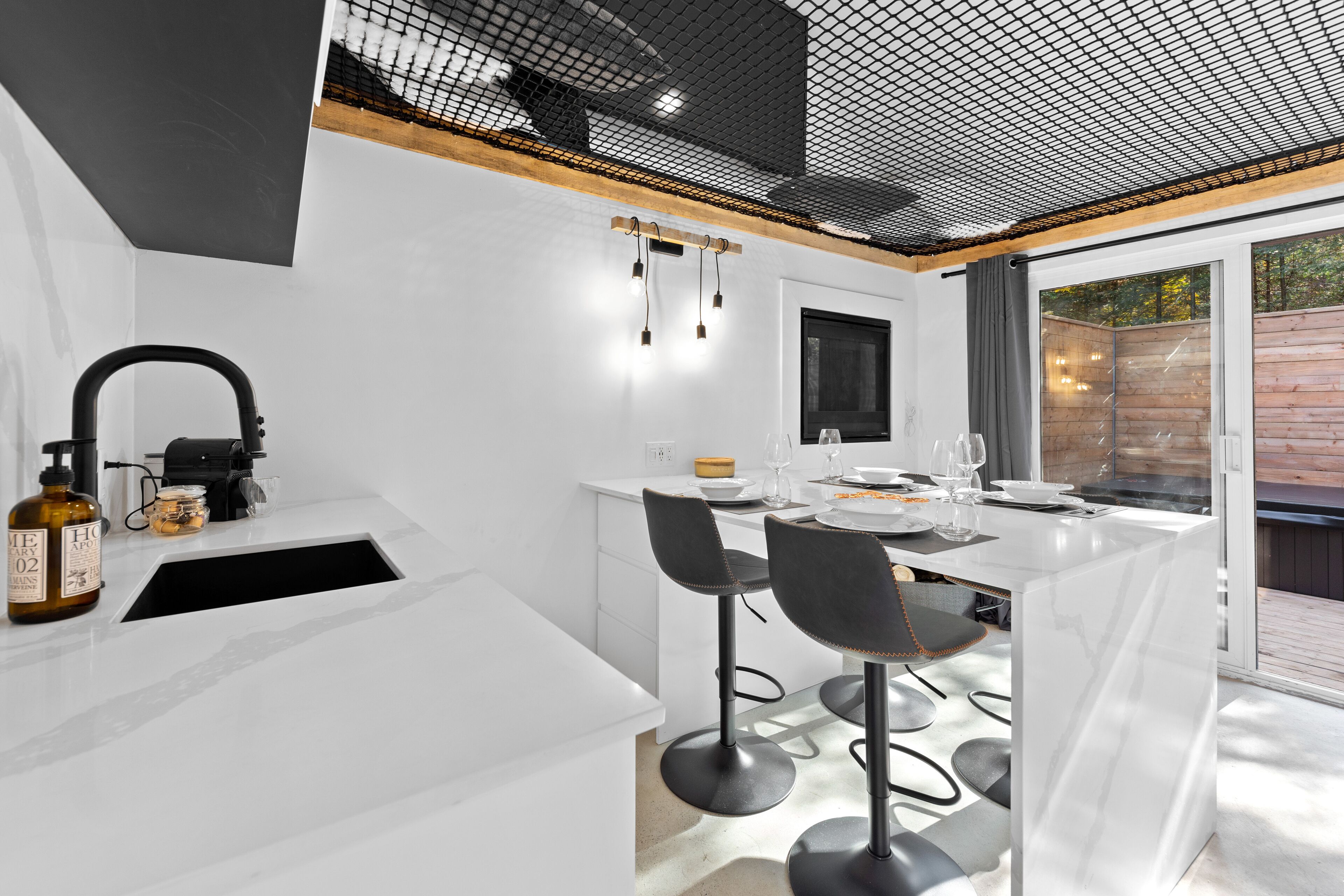 A modern kitchen with white countertops, black bar stools, and a large window.