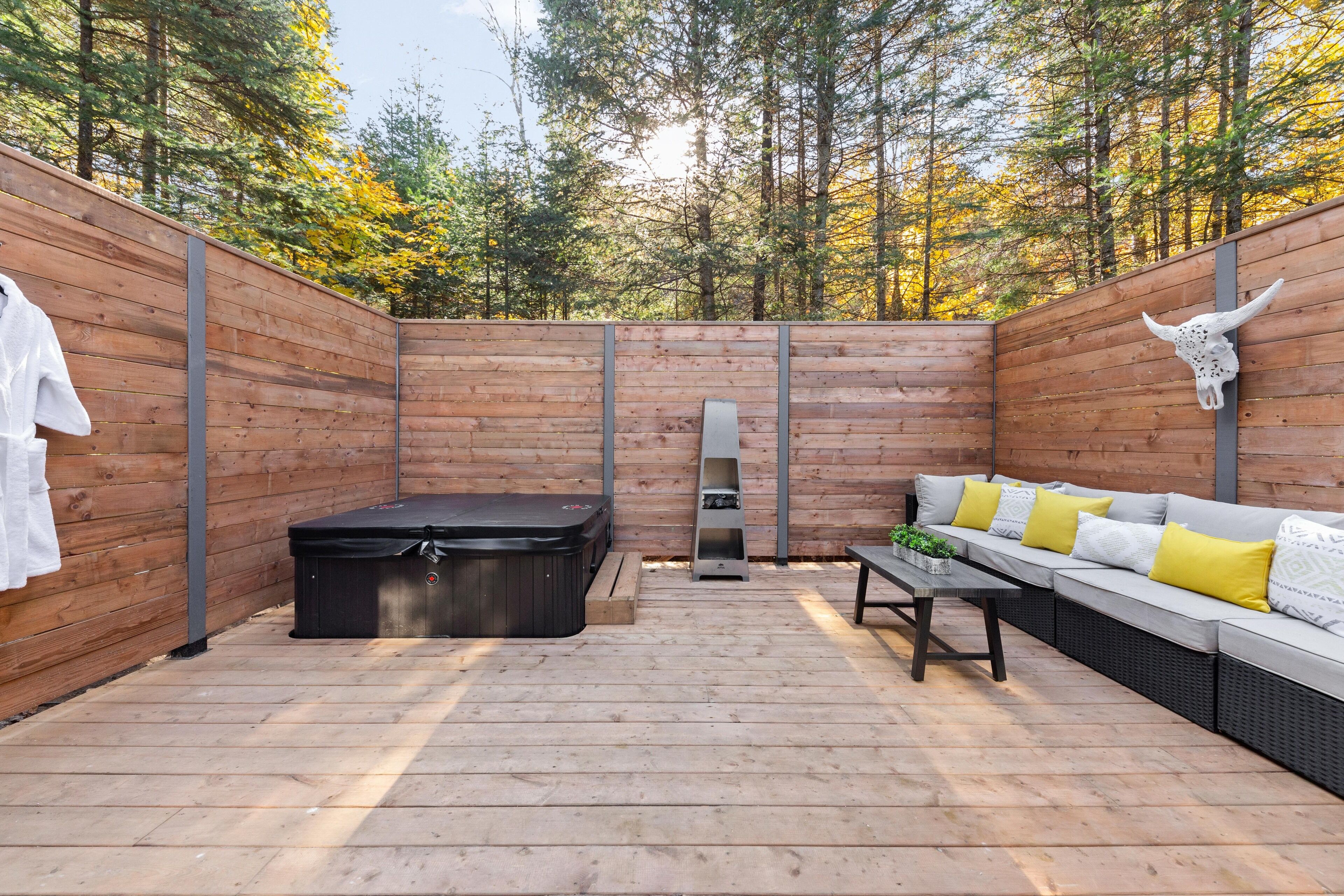 Une terrasse en bois avec un jacuzzi, un canapé avec des coussins et une décoration représentant un crâne de taureau.
