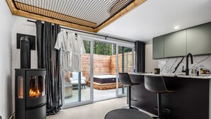 Una cuina moderna amb una estufa de llenya, una zona de menjador amb dues cadires i una porta corredissa de vidre que dona a una zona d'estar a l'exterior.