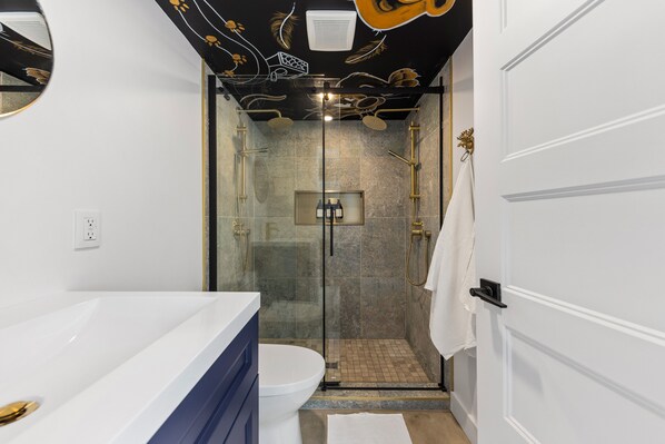 Un baño moderno con ducha acristalada, inodoro blanco y tocador azul.