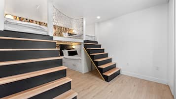 A modern interior with a staircase leading to a loft bedroom, featuring a unique ceiling design and a cozy seating area.