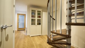 A staircase with a wooden handrail and metal balusters, leading to a landing with a white cabinet and a door with a window.
