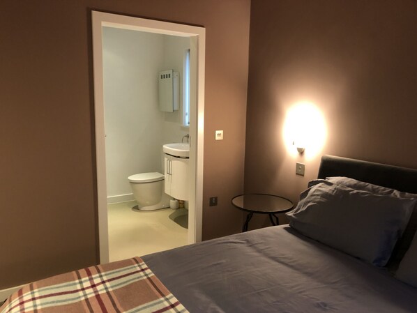 Una camera da letto con un letto, un comodino, una lampada e vista su un bagno con il water e un lavandino.
