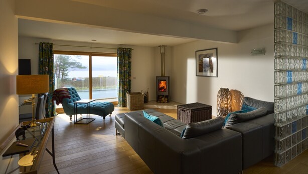 A living room with a sofa, a table with a lamp, a fireplace, and a view through a large window.