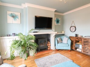 A living room with a fireplace, a television, a clock, and a blue armchair.