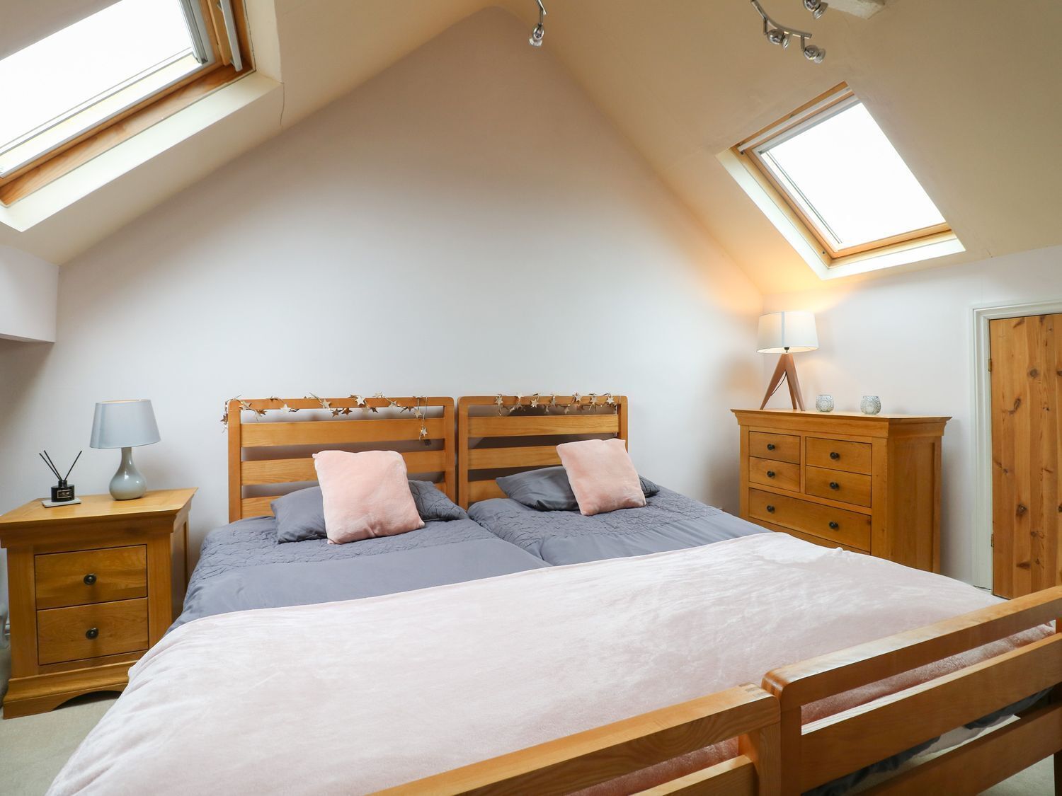 A bedroom with a sloped ceiling, skylights, a bed with a wooden headboard, bedside tables with lamps, and a wooden dresser.