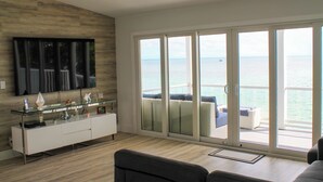Una sala de estar moderna con un amplio ventanal corredizo que da a un balcón con vistas al mar.