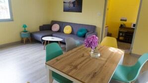 A modern living room with a wooden dining table, colorful chairs, a grey sofa with cushions, a small round table, and a wall-mounted picture. - House with pool near Verbania and Lake Maggiore (Cissano)