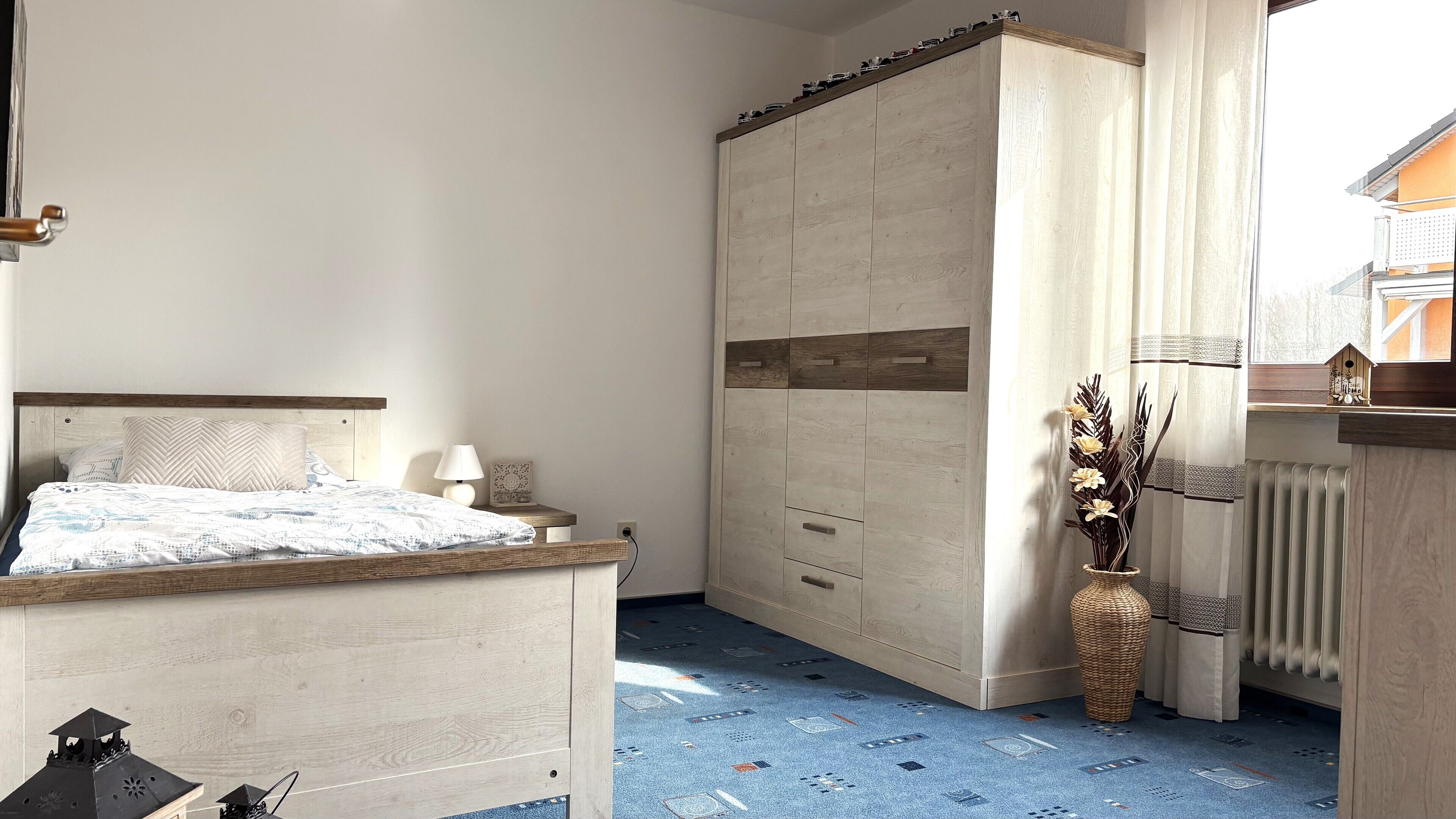A bedroom with a bed, bedside table, lamp, and a wardrobe.