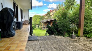 A patio with a tiled floor, a covered grill, and a wooden deck. - Spacious holiday apartment with terrace and garden (Bindlach)