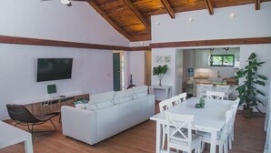 A modern living room with a white sofa, a dining table with white chairs, a TV mounted on the wall, and a ceiling fan. - Cozy Entire Villa with Picuzzi (La Romana)