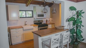A compact kitchen with white cabinets, a wooden countertop, a microwave, and a stove. There are two hanging pendant lights and a large green plant. - Cozy Entire Villa with Picuzzi (La Romana)