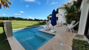 A swimming pool with a clear blue water, surrounded by a patio area with white lounge chairs and a blue umbrella. - Cozy Entire Villa with Picuzzi (La Romana)