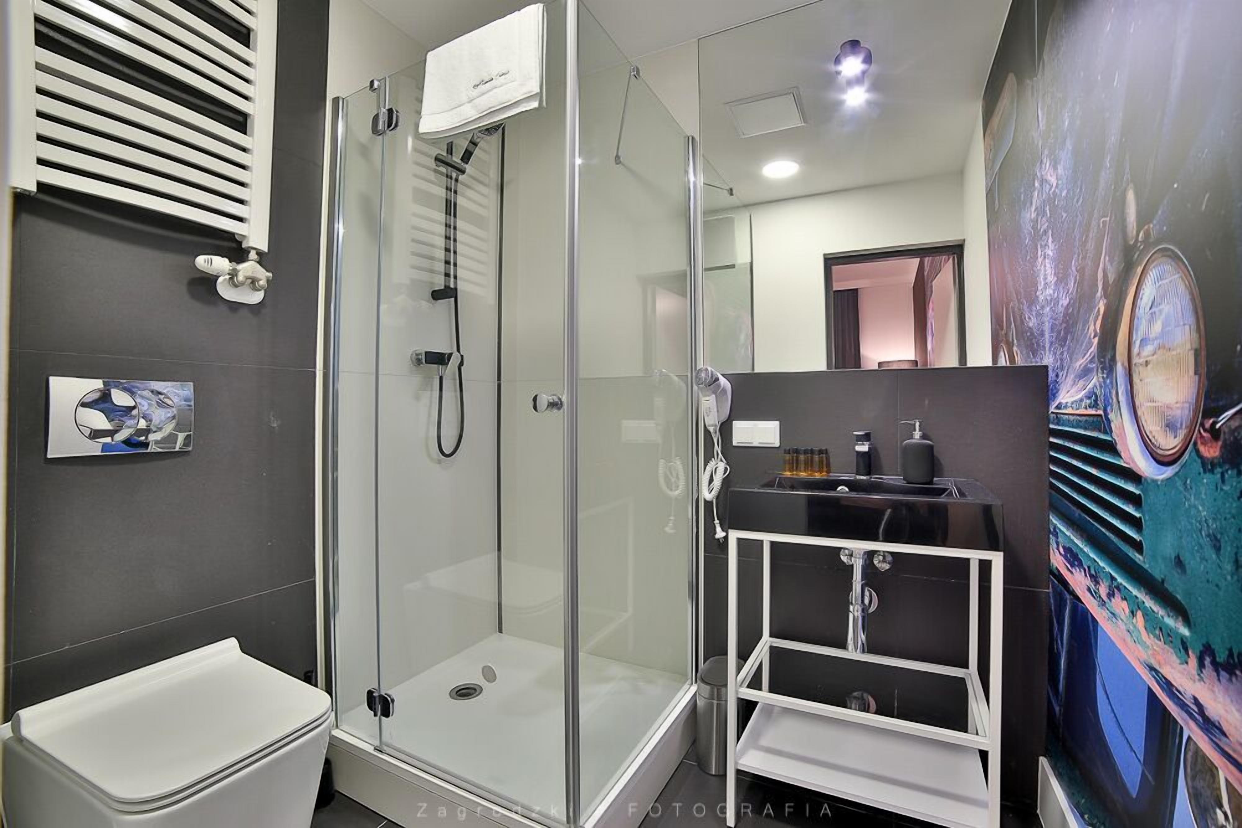 Een moderne badkamer met een douche met glazen wand, een wit toilet en een zwart wastafelmeubel met spiegel.