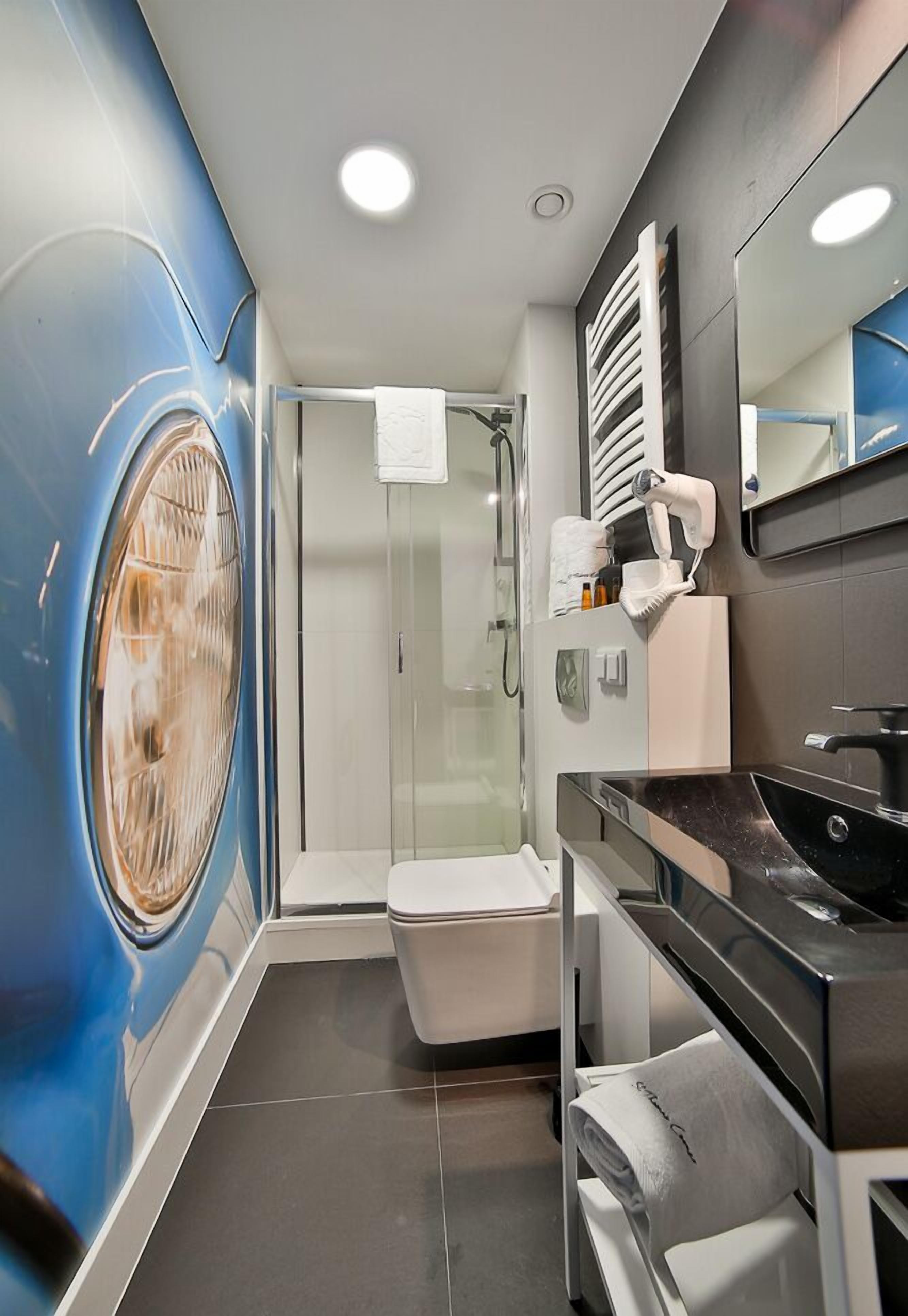 Un baño moderno con un espejo grande, un lavabo negro, un inodoro y una cabina de ducha de vidrio.