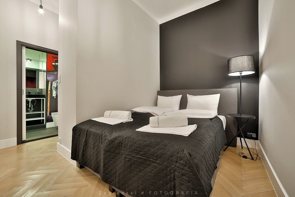 Un dormitorio moderno con una cama grande, una lámpara de noche y vistas a un baño con ducha e inodoro.