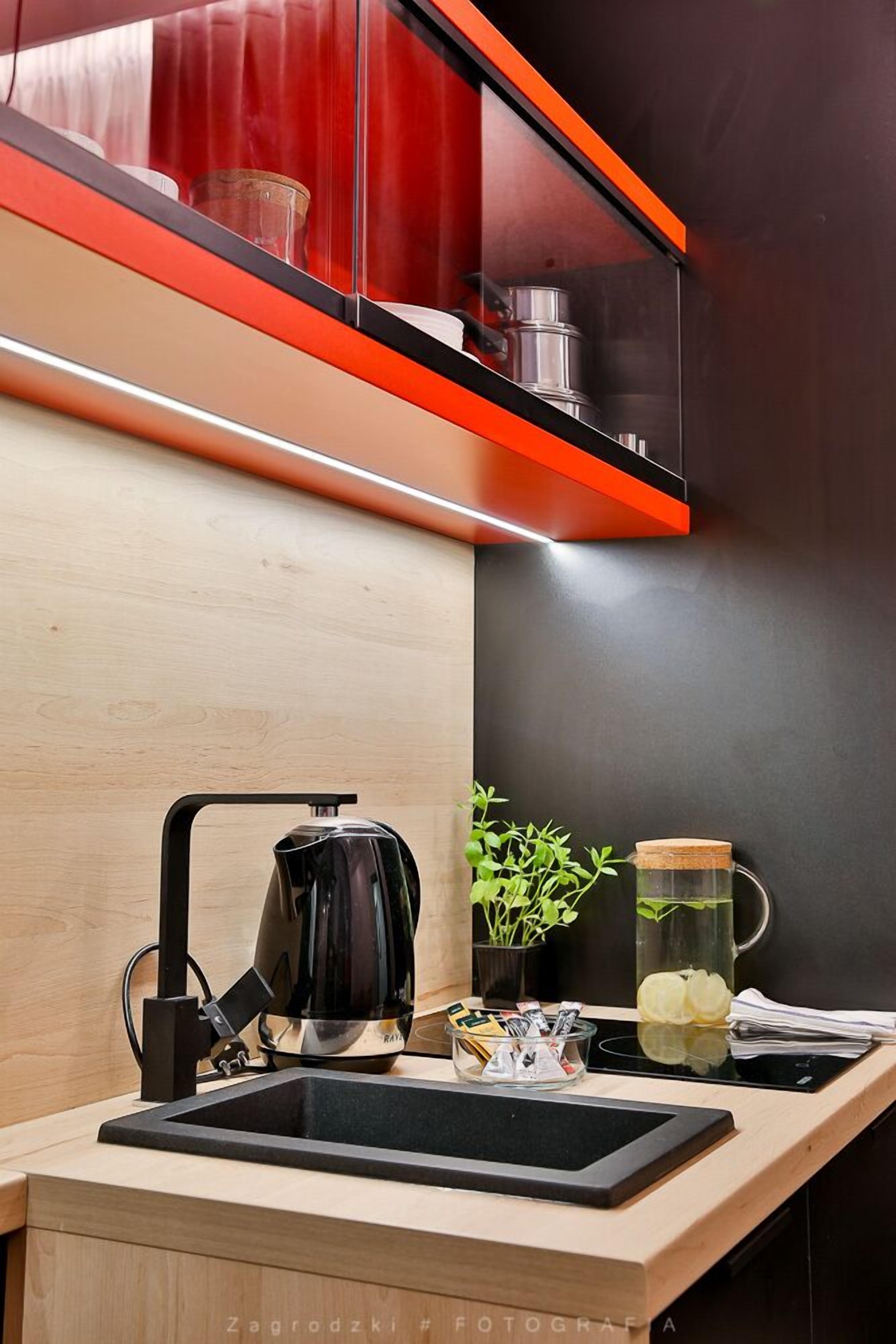 Une cuisine moderne avec une bouilloire noire, un pichet en verre et une petite plante posée sur le plan de travail.