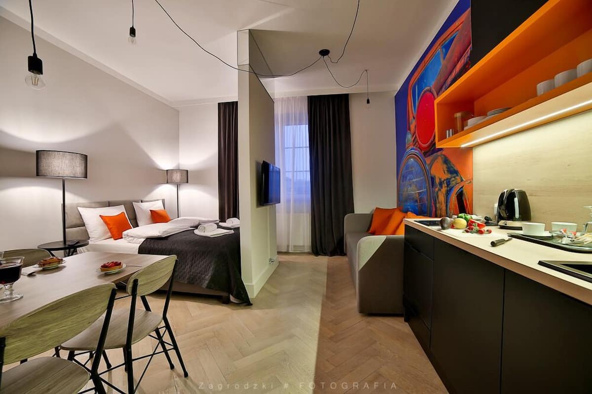 Una habitación de hotel moderna con zona de comedor, sofá, televisor y encimera de cocina.