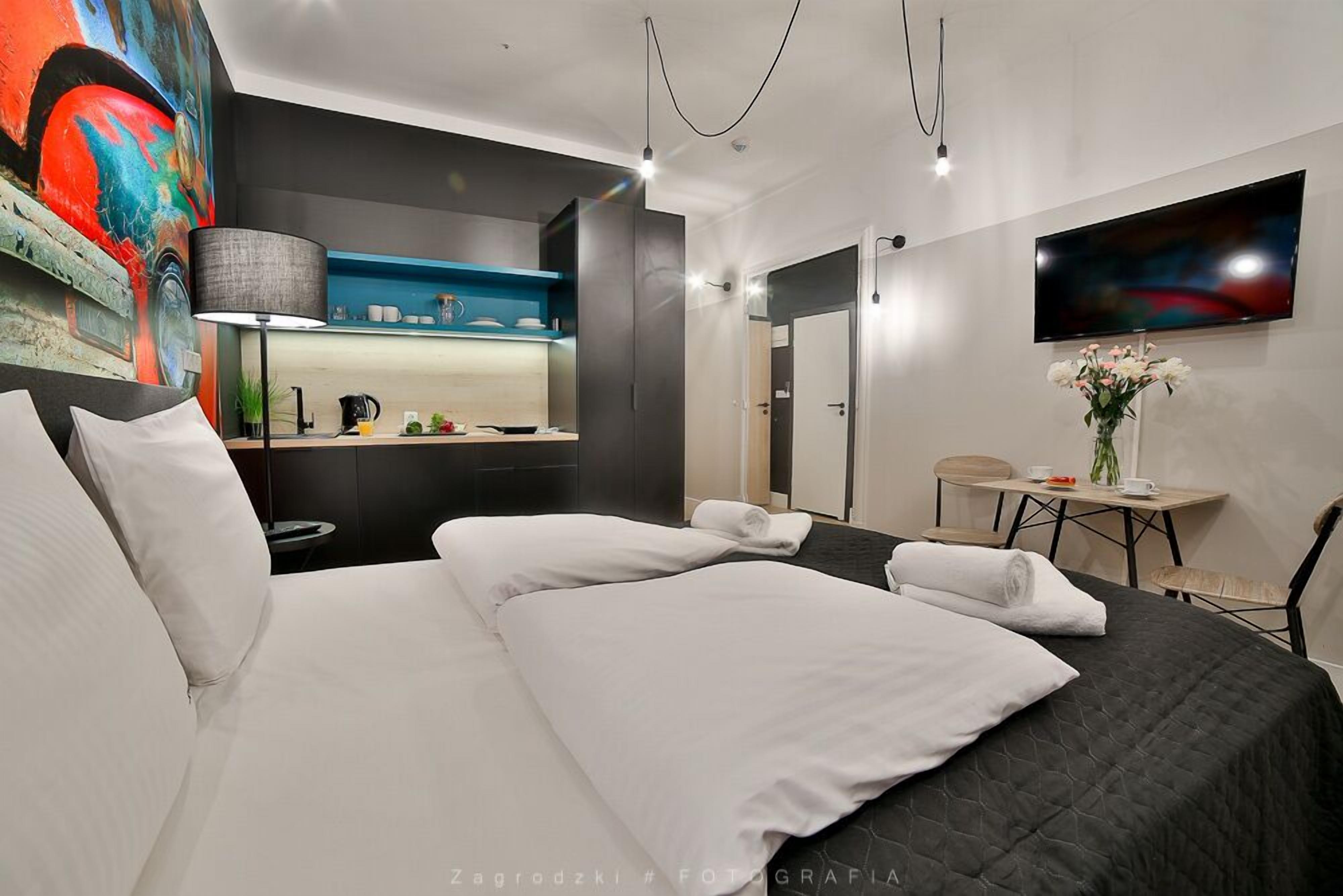 A modern hotel room with a large bed, a small desk, a TV, and a painting on the wall.