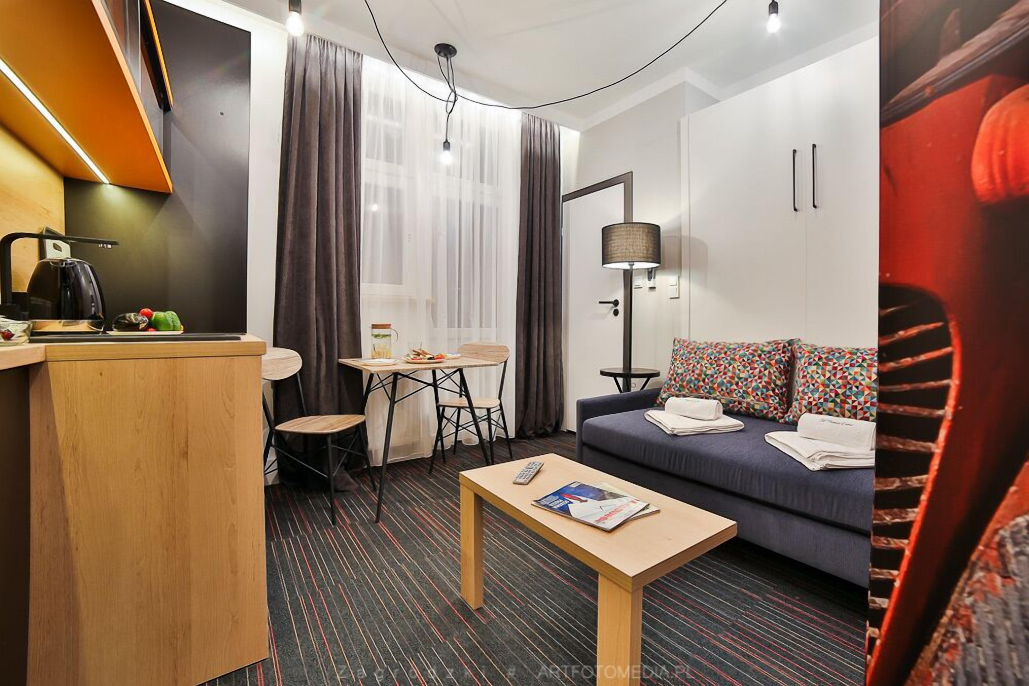 Une chambre d'hôtel compacte comprenant un coin cuisine, un canapé avec des coussins à motifs, une petite table à manger et un lit simple.