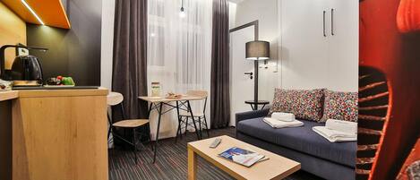 Une chambre d'hôtel compacte comprenant un coin cuisine, un canapé avec des coussins à motifs, une petite table à manger et un lit simple.