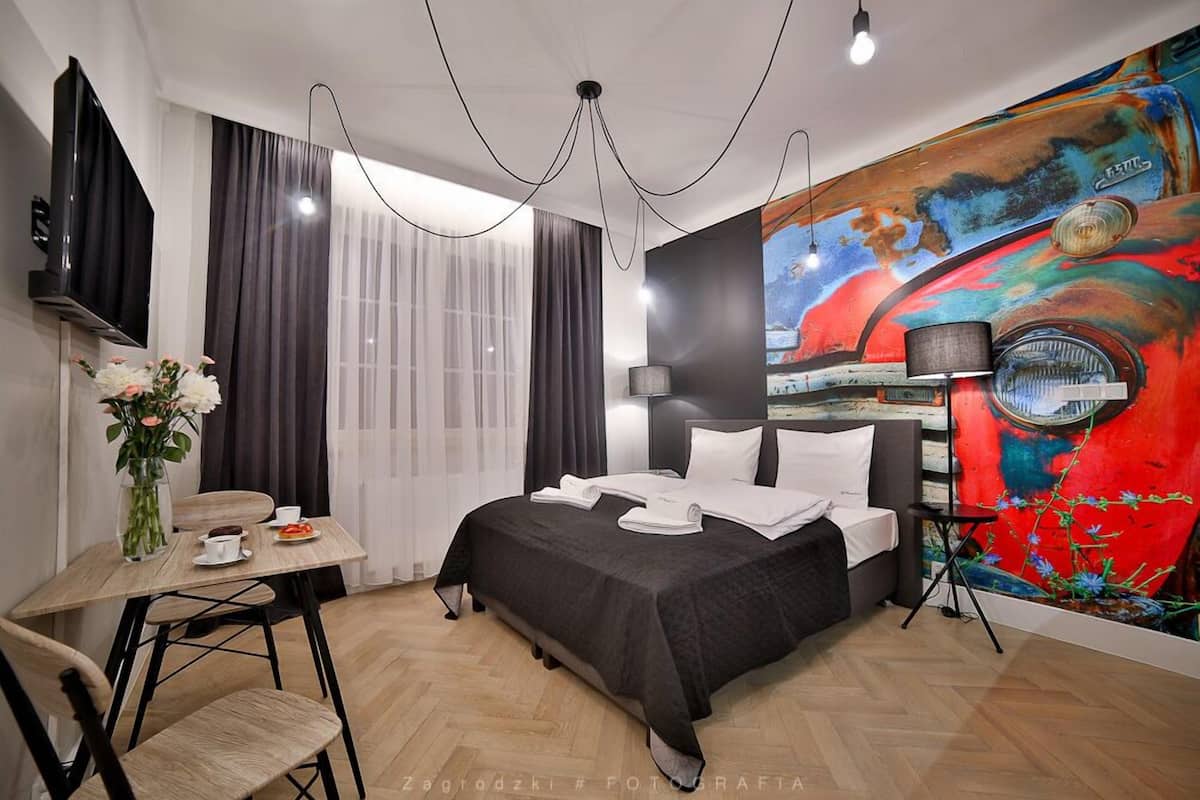 Habitación de hotel moderna con una cama grande, un escritorio con silla, televisión y un mural abstracto y llamativo en la pared.