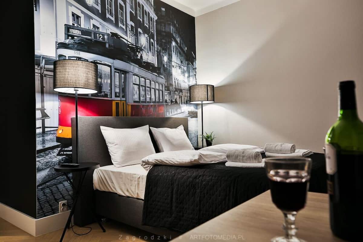Una habitación de hotel con una cama, dos lámparas de noche, una botella de vino y una copa de vino.