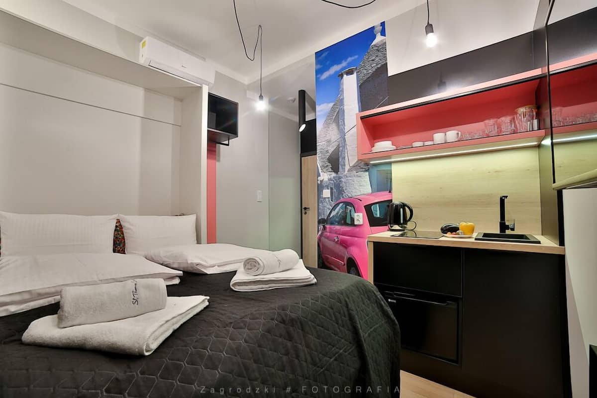 Una habitación de hotel moderna con una cama, un pequeño rincón de cocina y un cuadro de un coche rosa en la pared.