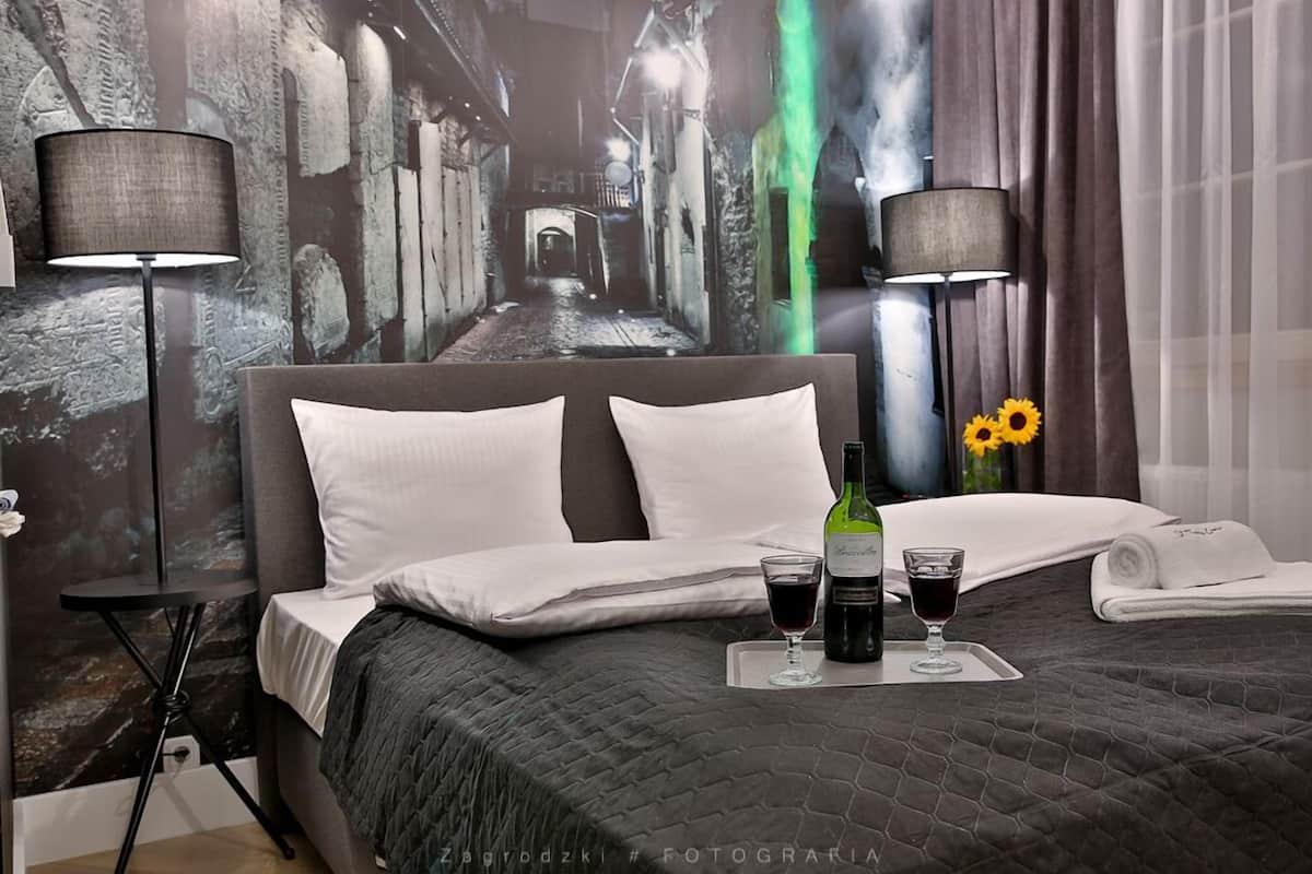 Habitación de hotel con una cama grande, dos lámparas de noche, una mesita de noche, una bandeja con una botella de vino y dos copas, y un jarrón con girasoles.