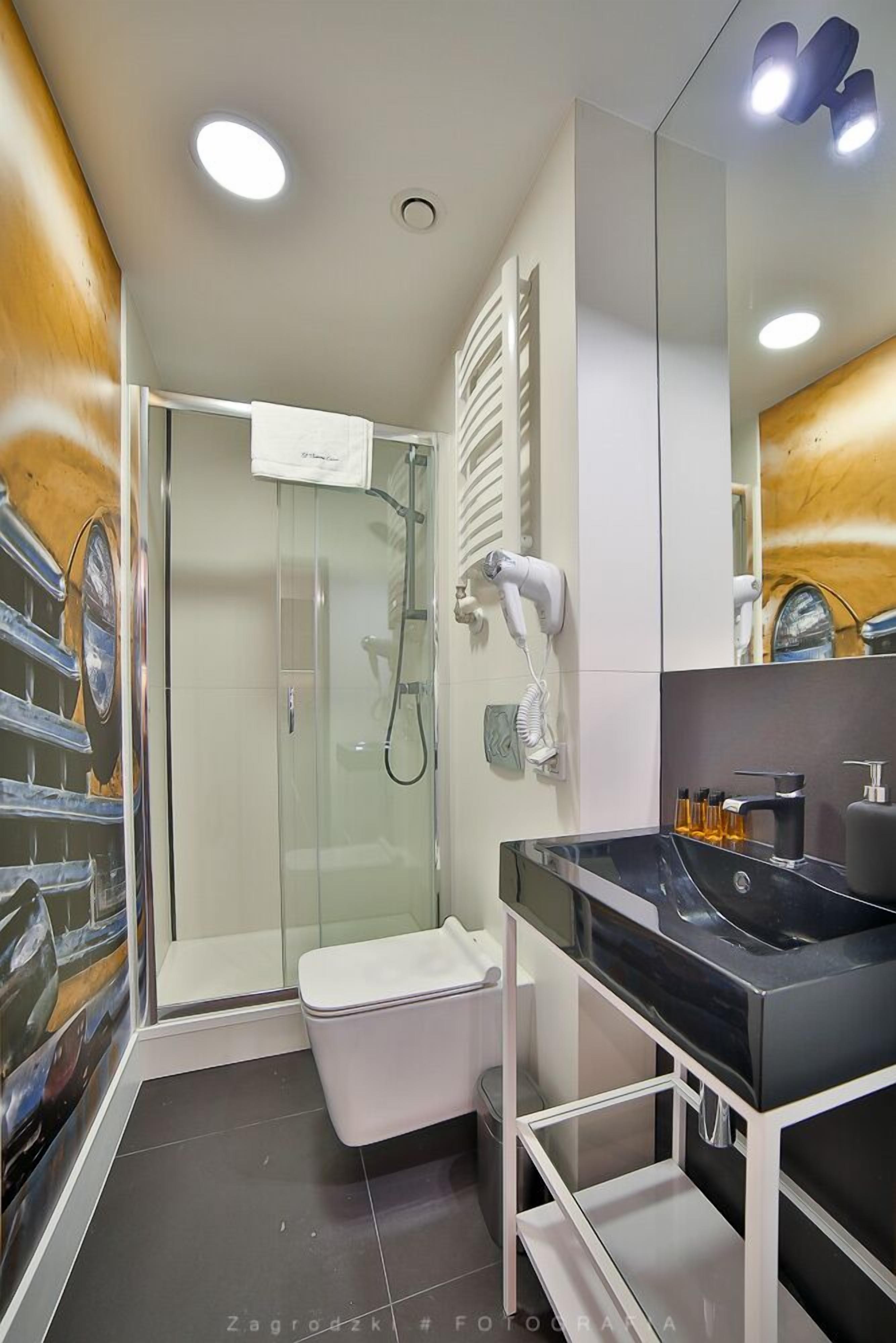 Une salle de bain moderne avec une douche à l’italienne en verre, des toilettes blanches, un lavabo noir et un miroir.