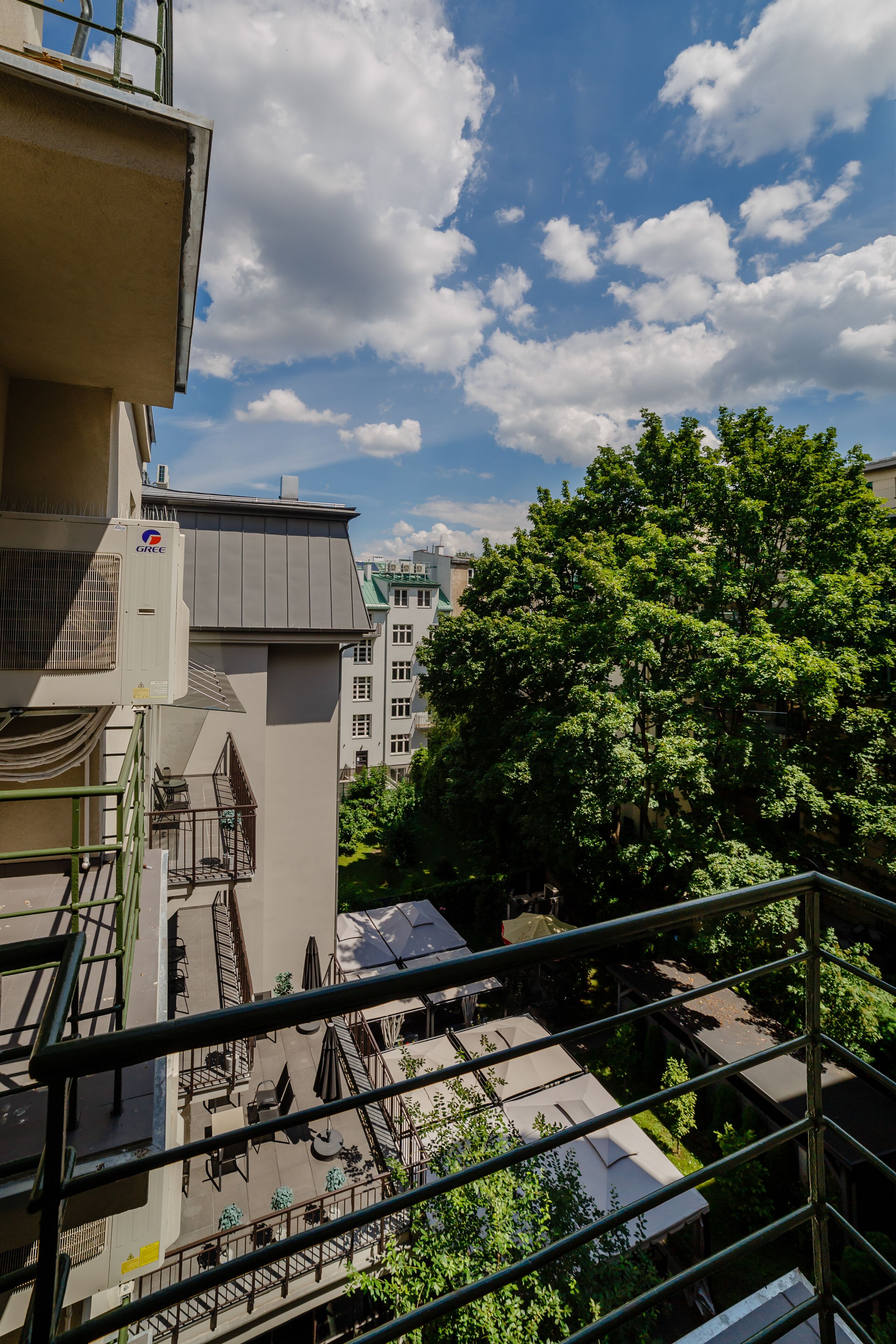 Een dakterras met buiten zitplaatsen, uitzicht op een straat met bomen, en een gebouw met een GREE airconditioner.