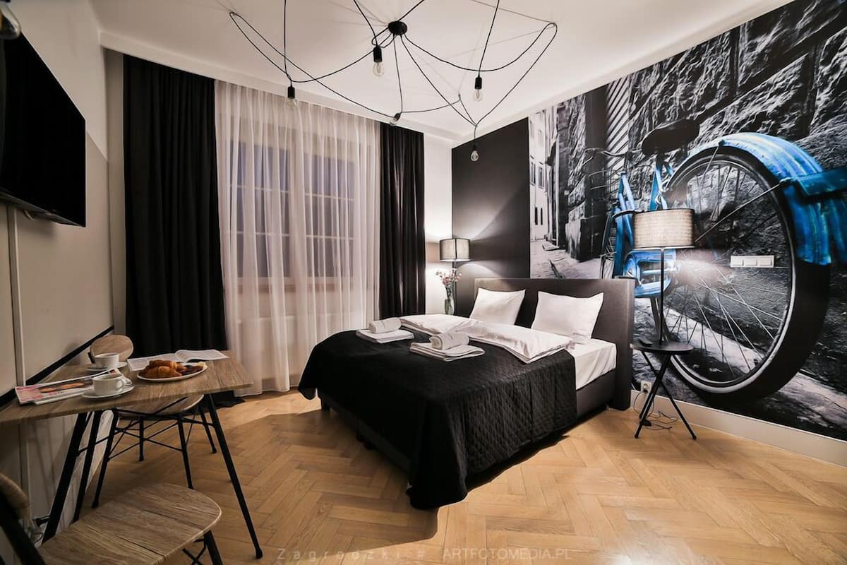 Una habitación de hotel con cama, escritorio con silla, televisor y un ventanal con cortinas.