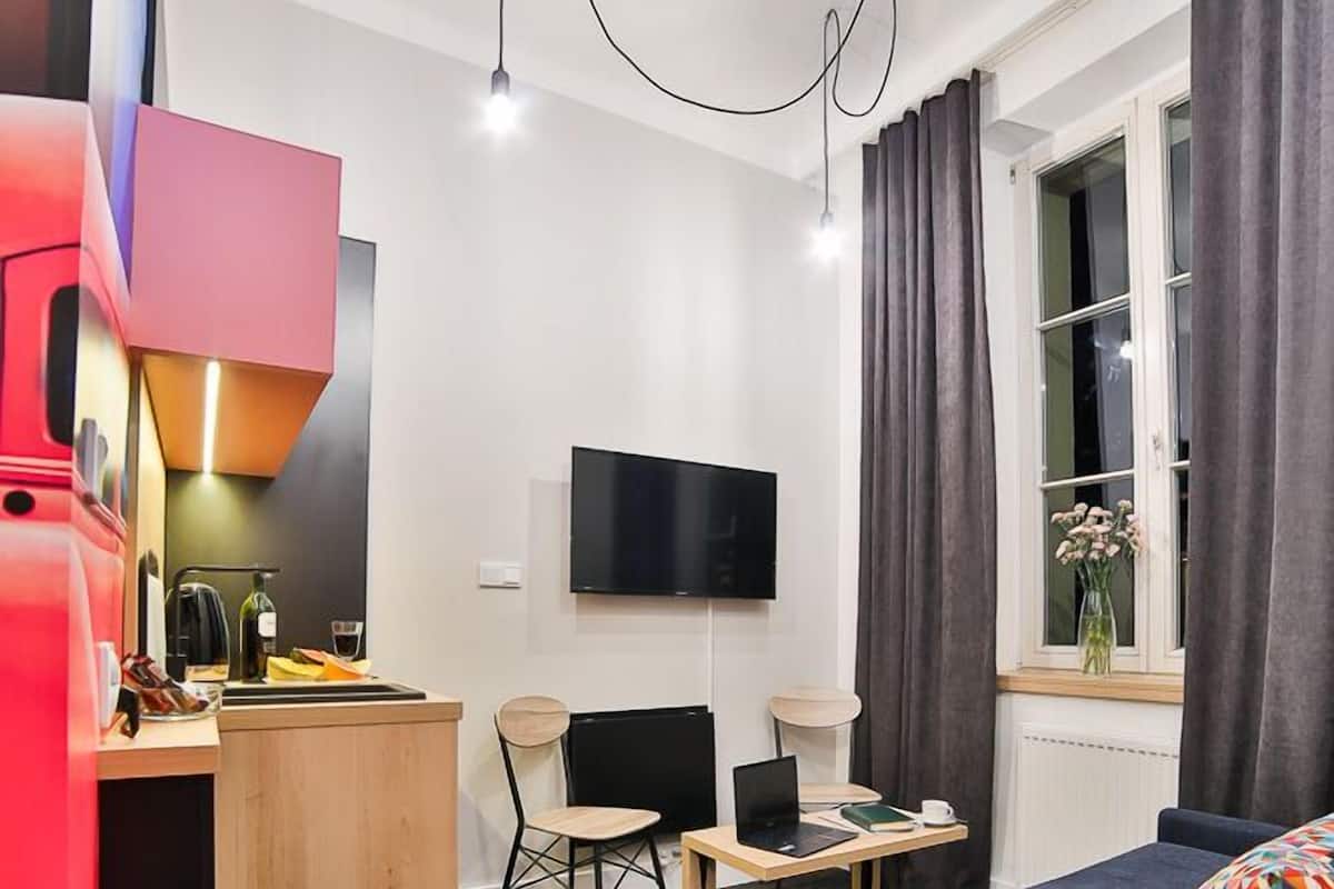 Habitación de hotel con cama, escritorio, silla, televisor y ventana con cortinas.