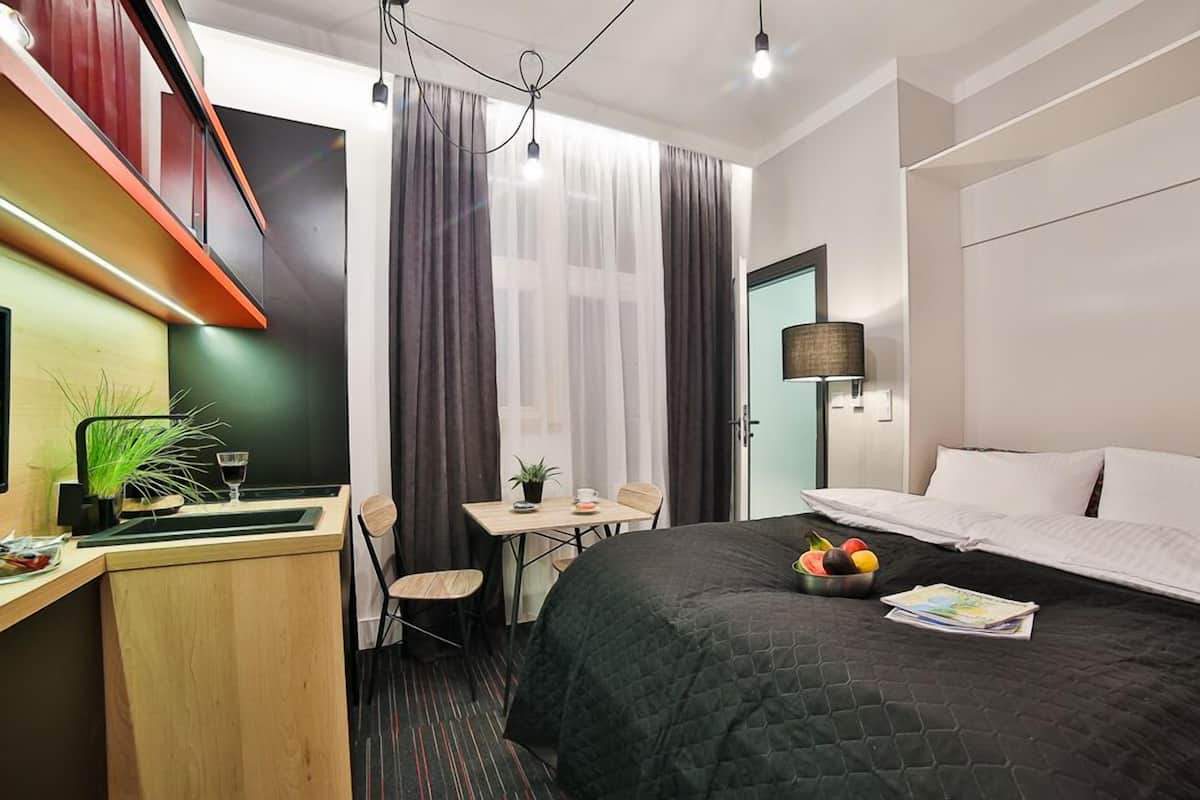 Habitación de hotel con una cama, un escritorio con una silla, una mesita con una planta y una ventana con cortinas.