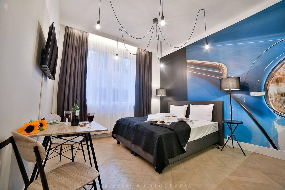 Una habitación de hotel moderna con cama, escritorio con silla, televisión y un ventanal con cortinas.