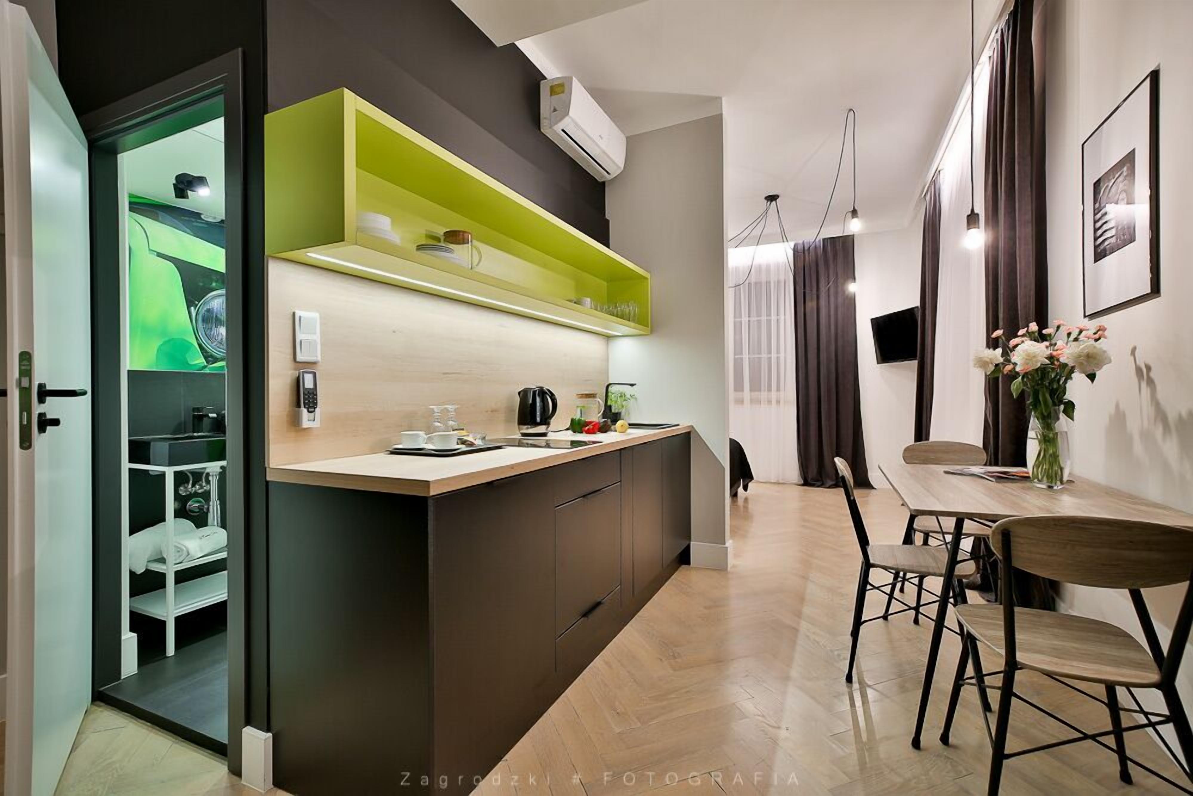 A modern kitchen with a central island, a dining area with a wooden table and chairs, and a view of a green car through a glass door.