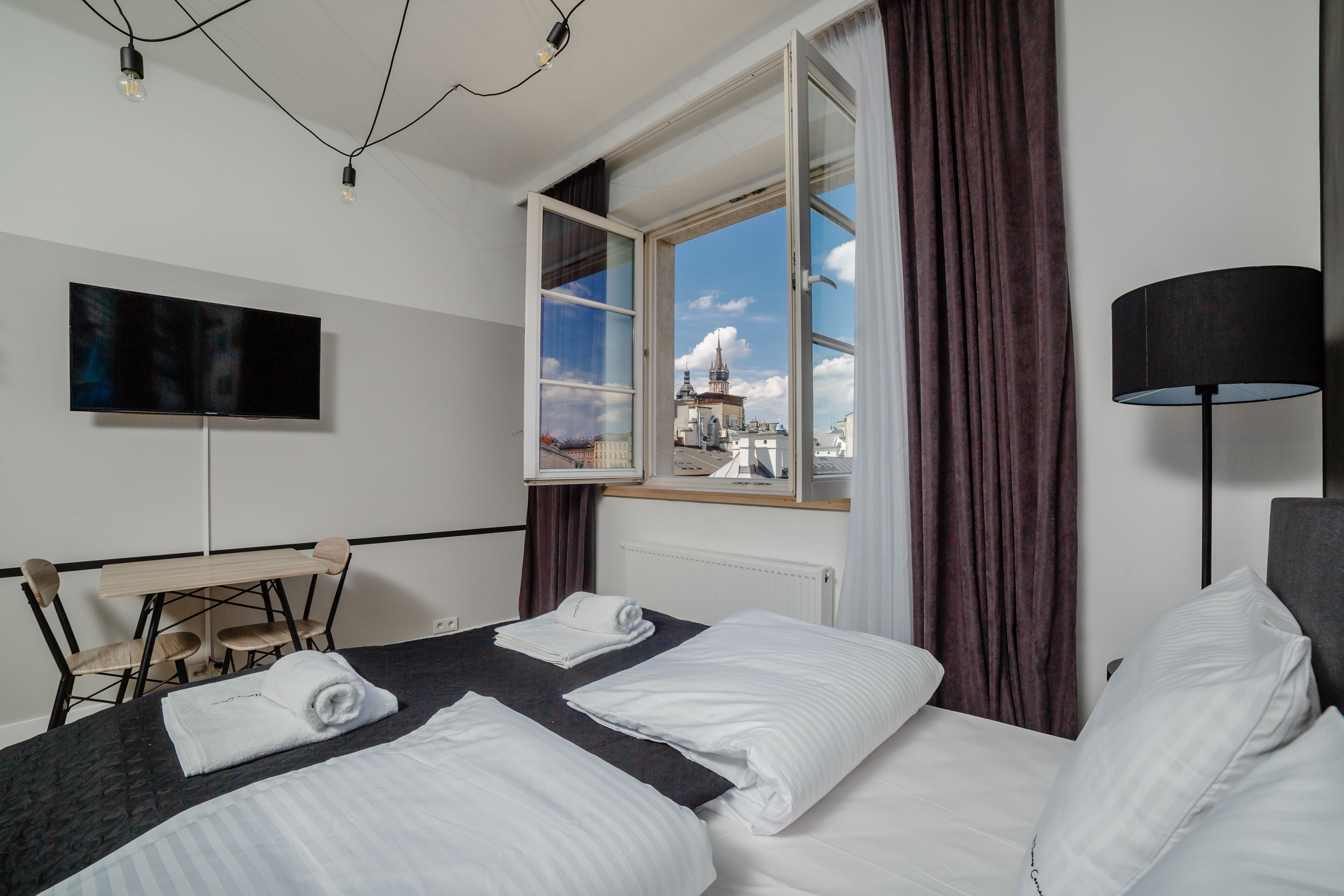 A hotel room with two beds, a desk, a chair, a TV, and a window with a view of a building.