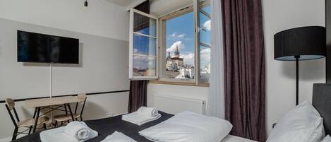 A hotel room with two beds, a desk, a chair, a TV, and a window with a view of a building.